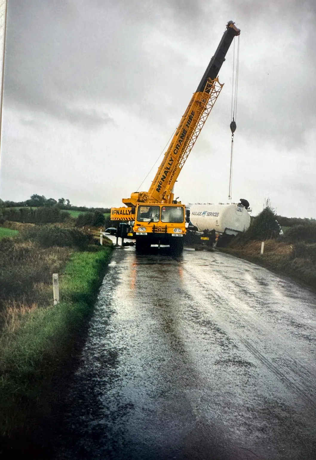 Archive photograph of a McNally’s mobile crane lifting a tank on a wet country road