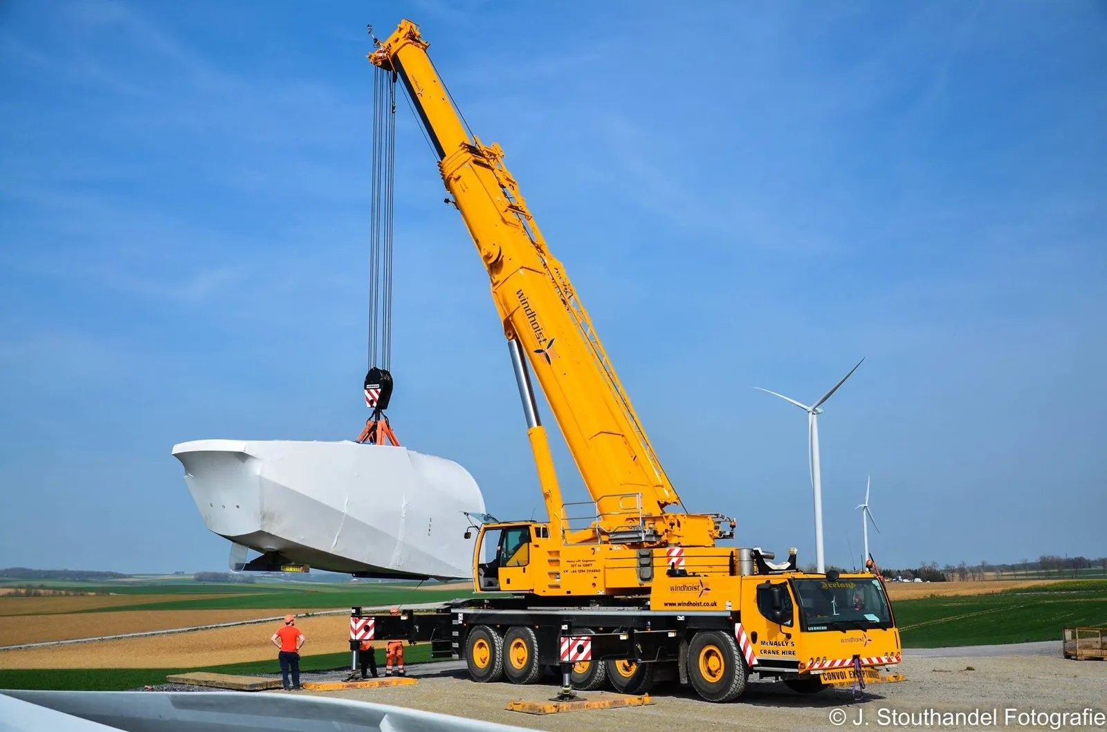 McNally’s all-terrain crane lifting a wrapped nacelle, with a finished turbine behind