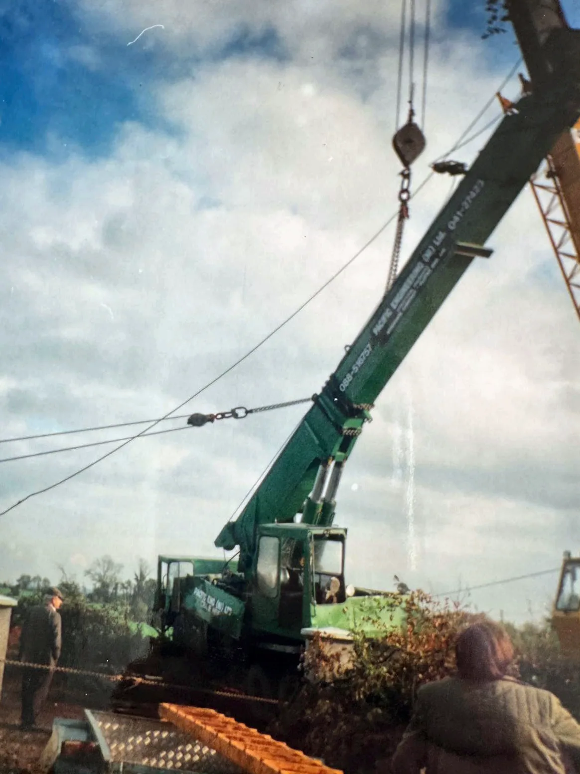 Archive photograph of an overturned green truck crane being chained and righted, with a yellow lattice crane alongside