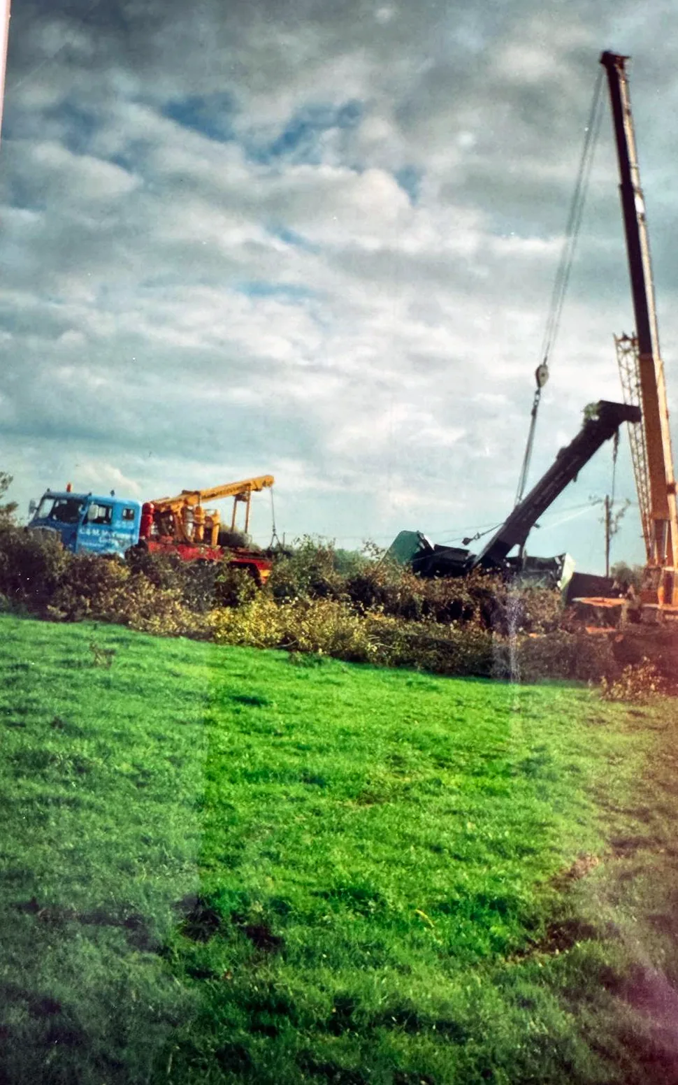 Archive photograph of a yellow telescopic crane and a recovery truck lifting an overturned crane out of a hedge