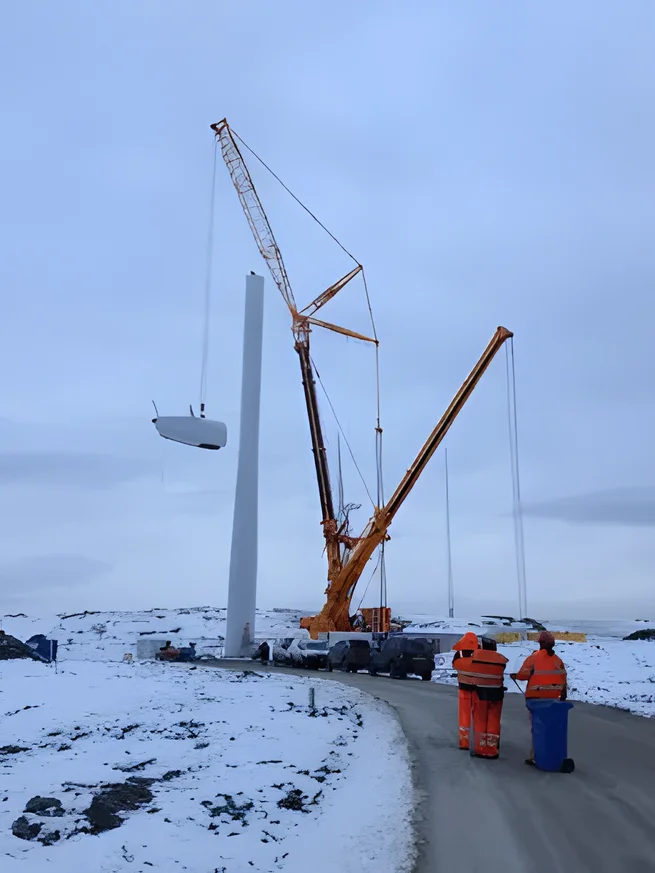 Two cranes lifting a nacelle on a snowy wind site at Armistead, with the crew watching from the track