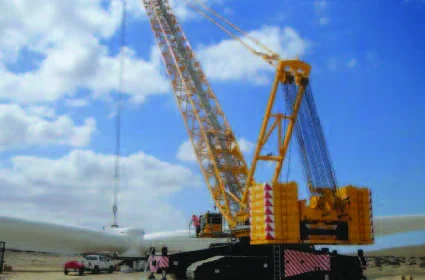 Crawler crane rigged beside turbine blades on a wind farm under a blue sky