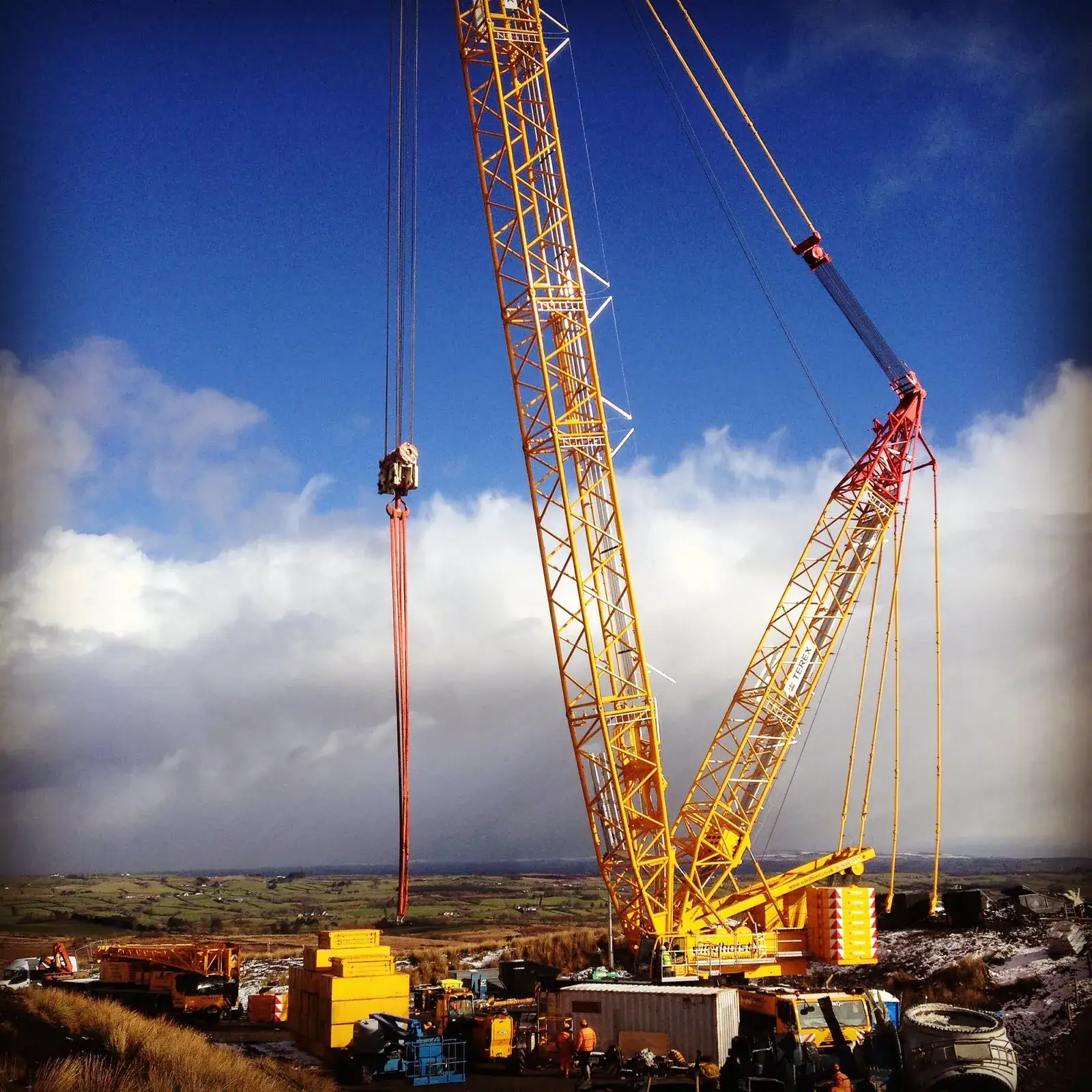 Yellow crawler crane on an upland wind site under a bank of cloud