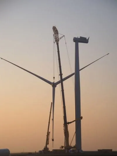 Crawler crane raising a three-bladed turbine rotor to the nacelle at sunset