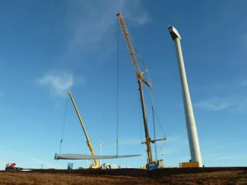 Two cranes lifting a turbine blade beside the tower at Gordonbush wind farm, Scotland