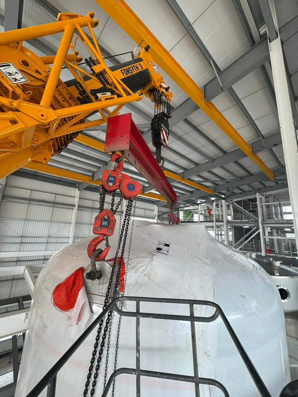 Crane hook and chain blocks over a large white component inside a factory