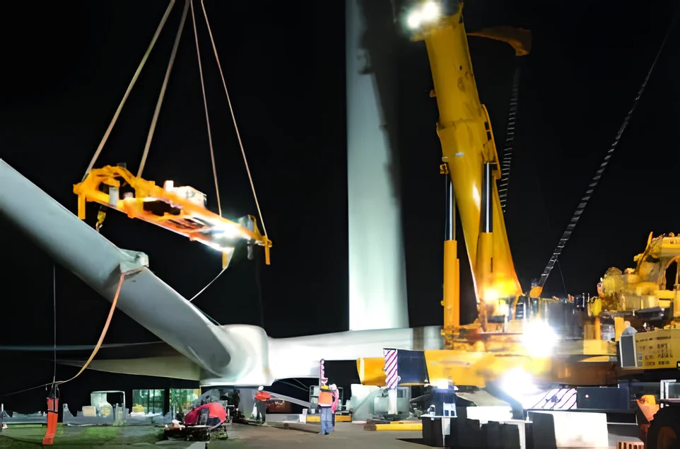 Night lift of a turbine blade with a spreader beam under floodlights