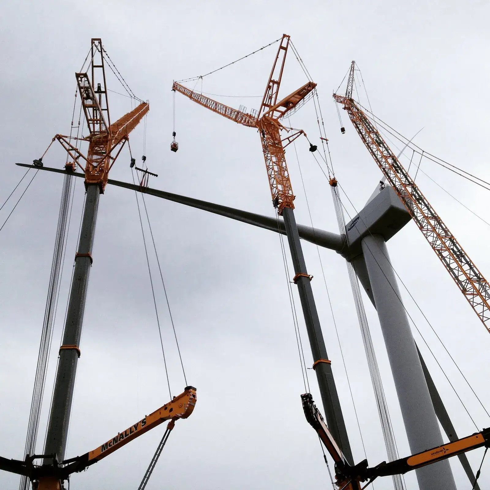 Looking up at three cranes working on a wind turbine tower