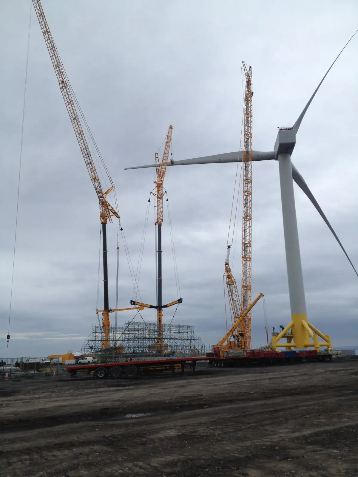 Three cranes positioned around a wind turbine under construction