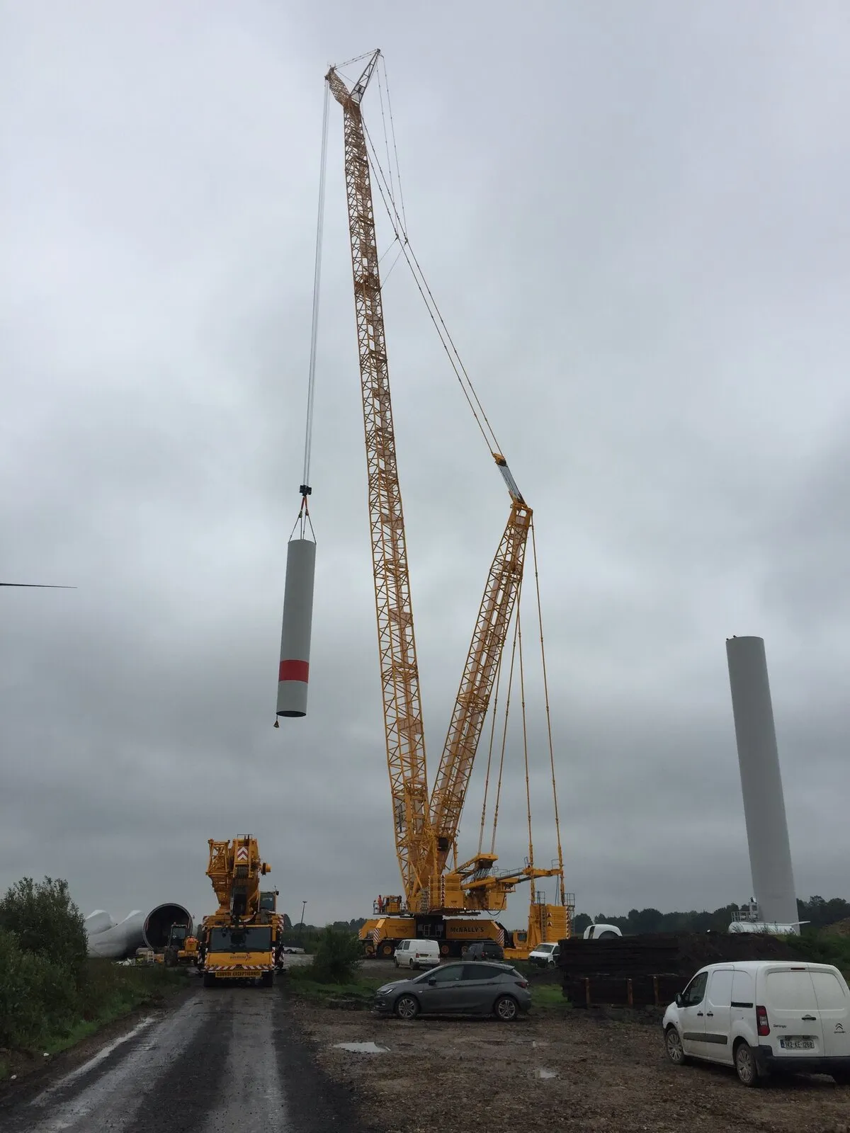 Crawler crane lifting a turbine tower section, with a finished tower behind