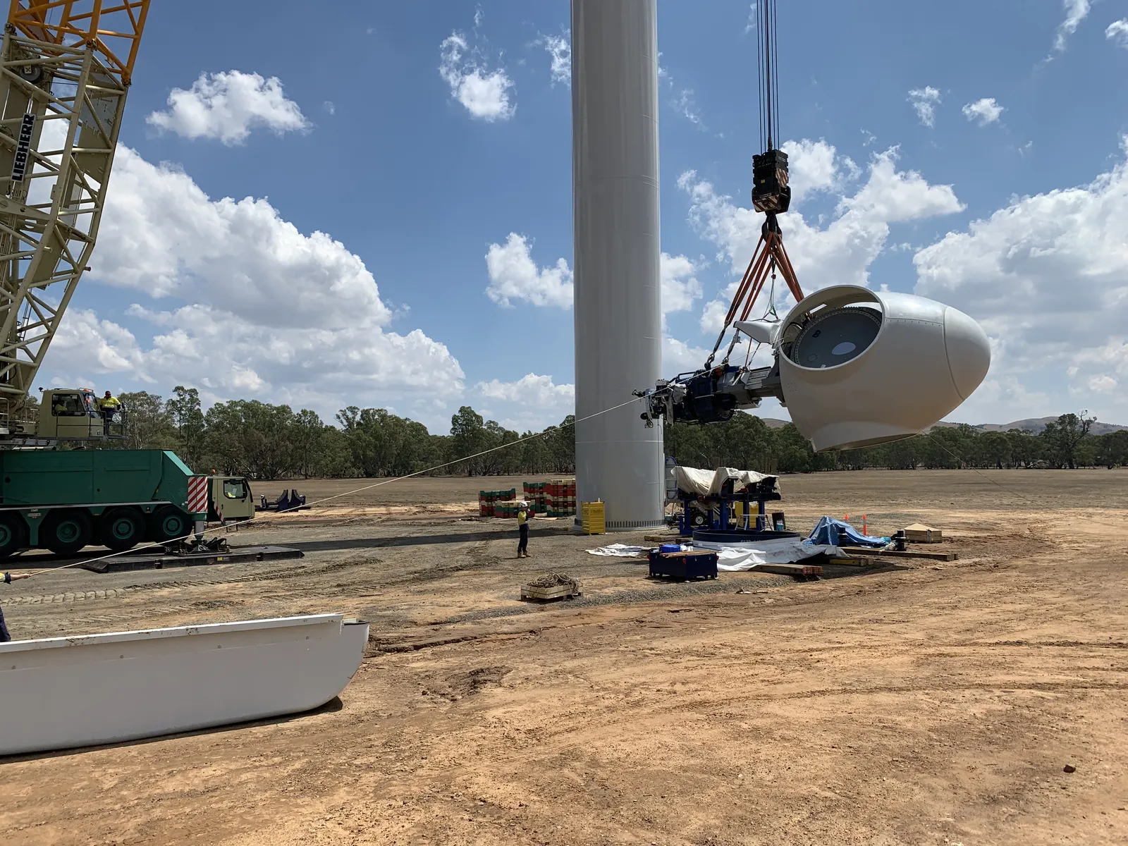 Lattice crane lifting a turbine nacelle beside the tower